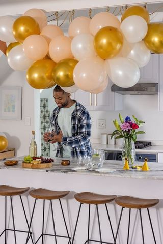 African american man arranging glassware at marble kitchen island under gold balloons