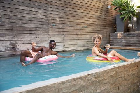 Couple lounging on inflatable rings in pool holding drinks enjoying summer relaxation