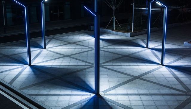Blue led poles casting geometric light beams across urban plaza at night