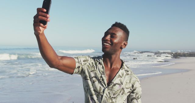 Smiling african american man taking selfie with smartphone on sunny beach by the sea. Summer, free time, relaxation, communication and vacations.