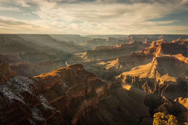 Breathtaking view of the Grand Canyon at sunset. Rocky cliffs are illuminated by the soft evening light, casting dramatic shadows and highlighting the rugged terrain. Perfect for use in travel brochures, nature magazine articles, wall art, calendar imagery, or advertisements promoting outdoor exploration and tourism.