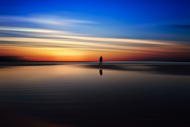 Lonely Person Standing on Beach at Sunset with Reflection in Water - Download Free Stock Photos Pikwizard.com