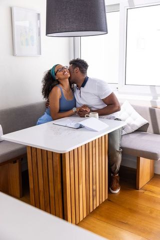 Black couple kissing and holding hands in bright cozy dining nook with coffee notebook