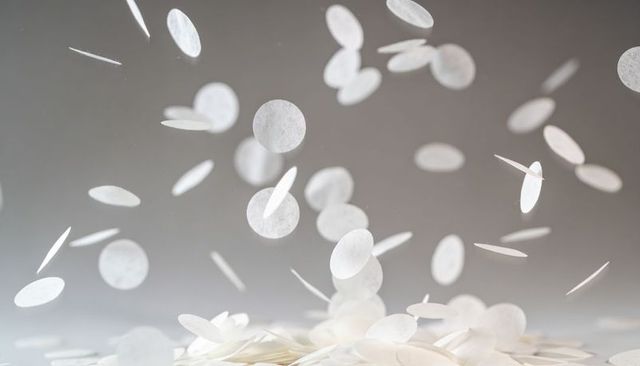 Floating white confetti discs drifting over tabletop with soft gray backdrop, motion blur
