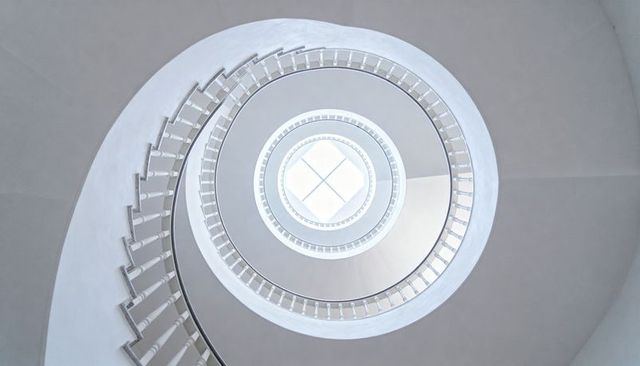 Spiral Staircase Leading Up to Skylight in Minimalist White Atrium with Geometric Symmetry