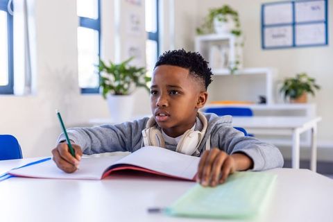 Focused african american boy studying in bright classroom wearing headphones