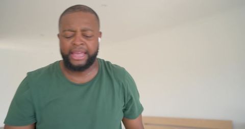 Emotional vocalist singing with earbuds in bedroom, eyes closed, green tee performance