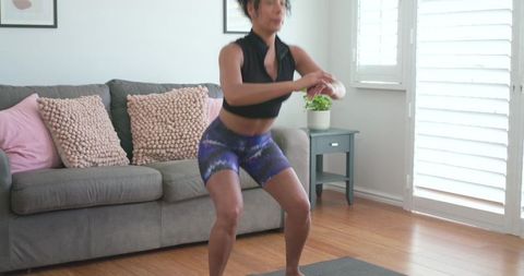African american woman performing squat workout in living room, home fitness session