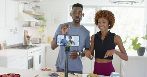Recording couple demonstrating healthy meal prep and post-workout snacks in bright kitchen