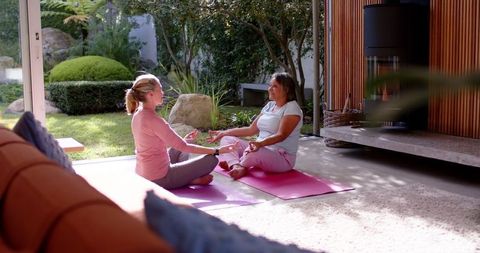 Senior Women Practicing Meditation at Home Near Garden and Fireplace