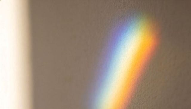 Sunlight casting rainbow prism on textured plaster wall with soft subtle gradient and warm tones
