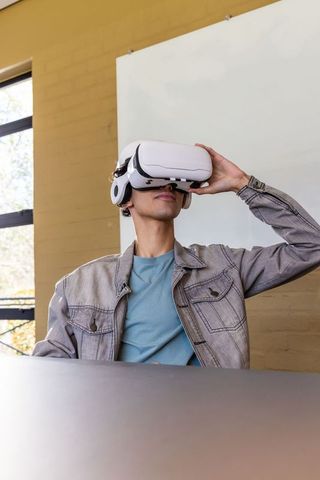 Asian student exploring virtual reality while adjusting white VR headset in modern classroom