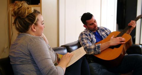 Man Playing Guitar While Woman Reading in Cozy Living Room