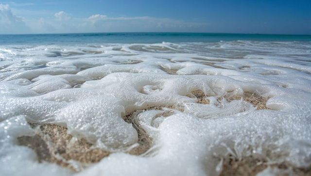 Seafoam Cascading Over Sand Grains on Turquoise Shoreline at Low Tide, Close-Up