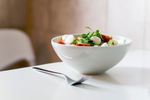 Fresh Caprese Salad Bowl with Mozzarella, Cherry Tomatoes and Greens on Minimalist White Table
