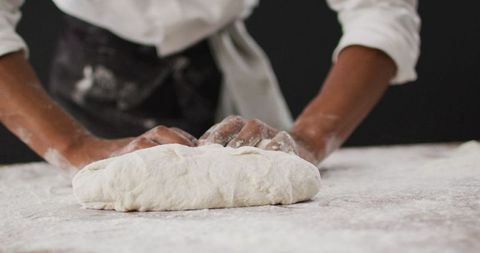 Chef kneading dough on floured surface in kitchen