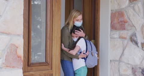 Mother and Daughter Embracing by Open Door Wearing Face Masks