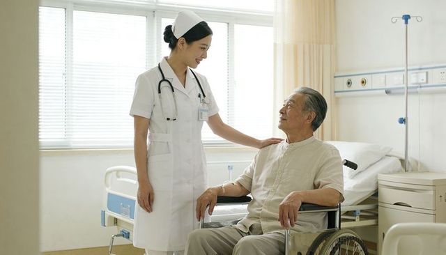 Nurse providing compassionate bedside care to elderly man in wheelchair hospital ward