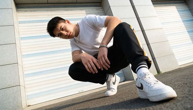 Low-angle streetwear portrait of crouching young man wearing white nike sneakers