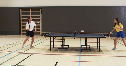 Female Athletes Competing in Dynamic Indoor Table Tennis Match