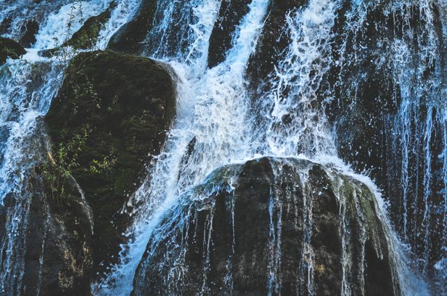 Close up view of a cascading waterfall flowing over rocky cliffs in a natural outdoor setting. Suitable for use in travel brochures, nature blogs, environmental posters, and websites promoting outdoor activities and natural beauty destinations.