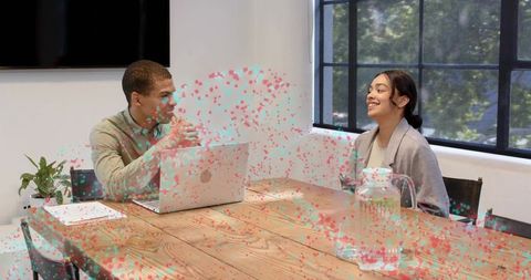 Colleagues collaborating in modern conference room, man gesturing at laptop, woman listening