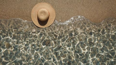 Straw sun hat on pristine beach with sparkling ripples