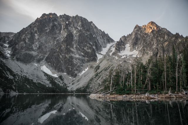 Pristine lake reflecting rugged mountain peaks at sunrise. Excellent for travel websites, nature blogs, landscape photography collections, promotional materials for outdoor gear, and environmental conservation campaigns.