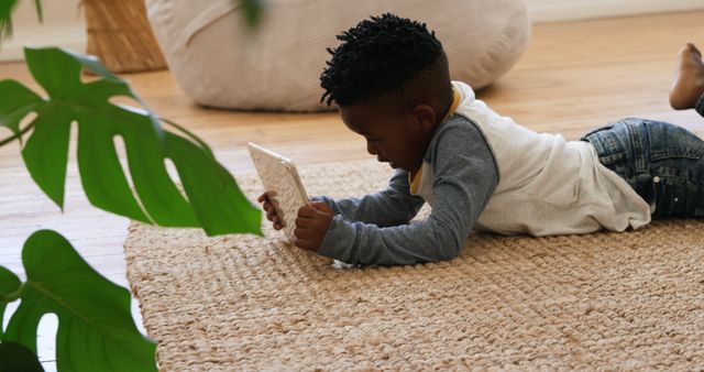 Child lying on a rug, using a tablet in a cozy home setting. Perfect for themes related to modern family life, childhood in the digital age, indoor living, kids' technology use, or advertisements for smart devices and educational apps.