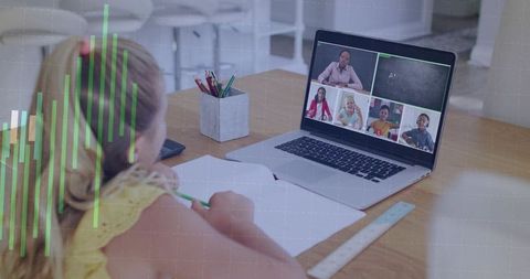 Girl attending virtual classroom while writing in notebook at home desk on laptop