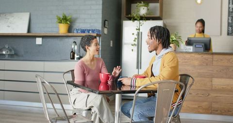 Diverse friends chatting over coffee at modern glass-top cafe table with barista and plants