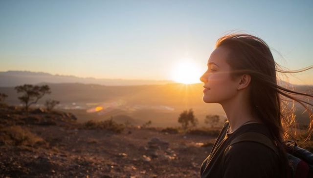 Young woman hiking at sunset on rocky ridge backlit by golden sun