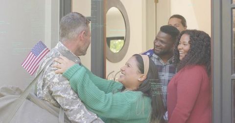 Soldier returning home hugging partner at doorway with American flag and family