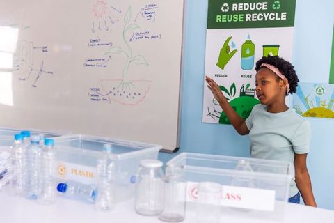 African american girl pointing at recycling bins in classroom teaching sorting and sustainability