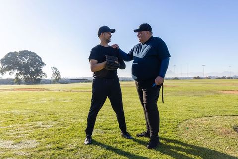 Coach guiding adult player glove technique on sunny baseball field, mentoring moment