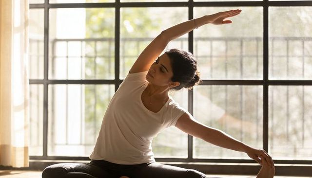 Woman practicing seated side stretch by sunlit grid window for home yoga and mindfulness