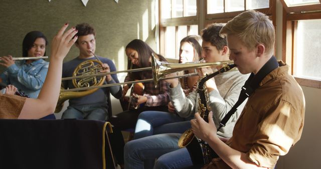 Group of diverse teenagers practicing musical instruments such as saxophone, trombone, trumpet, and French horn in a classroom ensemble. Ideal for educational content focusing on music education, team activities, and creative arts in schools. Suitable for advertisements, articles, or campaigns promoting music programs, cultural development, and extracurricular activities.
