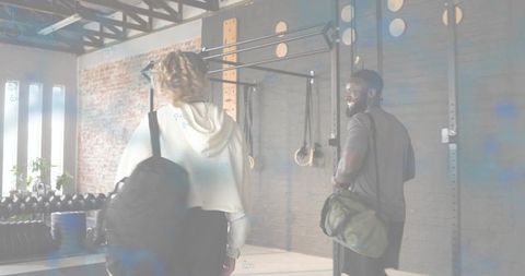 Training partners walking into industrial gym carrying backpacks and duffel bags