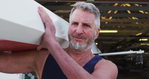 Senior Man Carrying Rowing Boat at Boathouse