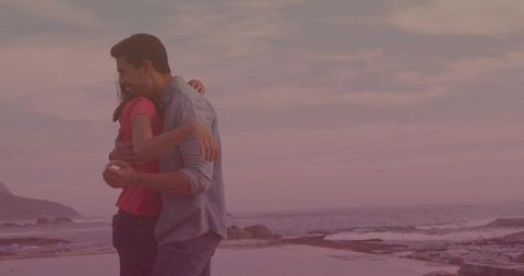 Couple hugging on rocky shoreline at pastel sunset holding seashell for romantic moment