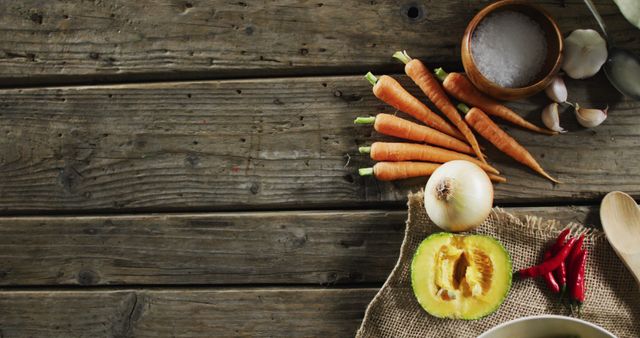This image depicts fresh vegetables and spices laid out on a rustic wooden table. It includes carrots, an onion, a piece of pumpkin, garlic, chili peppers, and a bowl of coarse salt. Useful for recipes, cooking blog posts, and articles focused on organic or healthy eating, as well as autumn and harvest themes.
