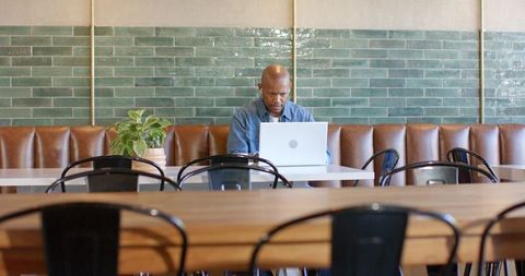 Focused man working on laptop in minimalist cafe with green tile wall and wood tables