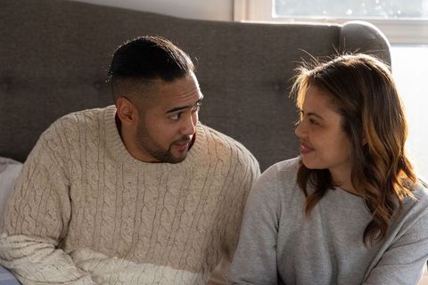 Couple sharing cozy morning moment on bed wearing knit sweaters