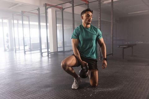 Kneeling athlete gripping kettlebell performing single-leg strength training in gym