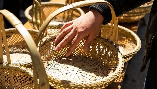 Right hand touching handwoven wicker basket at outdoor market stall in sunlight