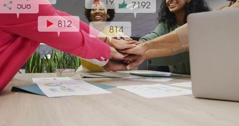 Colleagues Joining Hands at Conference Table Celebrating Teamwork and Social Media Wins