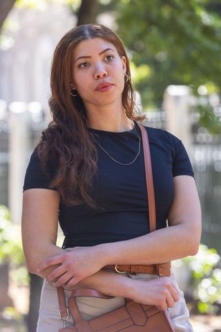 African american woman standing with arms crossed holding brown handbag in urban park