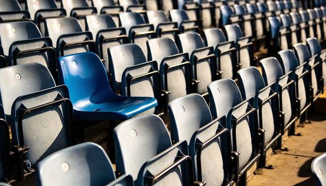 Bright blue seat standing out among empty stadium rows casting sunlit dramatic shadows