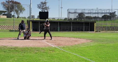 Male batter preparing to swing at home plate with catcher and umpire on sunny baseball field
