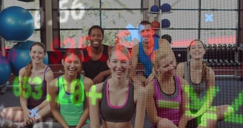 Diverse fitness class smiling and sitting on gym floor with weights and stability balls
